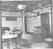 SA0492 - Christmas decorations in a room, showing a piano at the left, a stove, and rugs. Identified on the back.